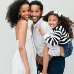 Smiling Black family: mother, father, and daughter posing together against a light background.