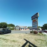 Commercial strip with signage for Quakerbridge Shoppes under a clear blue sky.