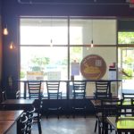 Modern cafe interior with large windows, artwork on the wall, and wooden tables.