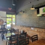 Modern restaurant interior with exposed brick, wooden paneling, and large windows overlooking an outdoor area.