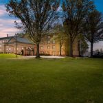 Historic hotel building behind a large green lawn under a colorful sunset sky.