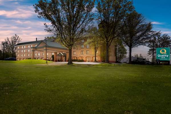 Historic hotel building behind a large green lawn under a colorful sunset sky.