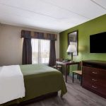 Modern bedroom with large bed, green accent wall, and mounted television.