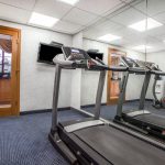 Treadmills in a gym with mirrored walls and an exit door.