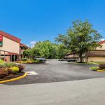 Hotel building with parking lot under a clear blue sky, surrounded by trees.