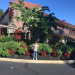 Young man stands in front of a large, red-roofed building with lush green landscaping.