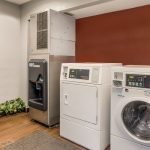 Commercial ice maker and white washing machines in a utility area.