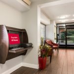 Wall-mounted TV in a modern hotel lobby area with seating and glass doors.