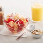 Bowl of strawberry and coconut parfait with orange juice, cinnamon, and almonds.