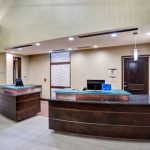 Modern hotel reception area with curved wooden desks and light-colored flooring.