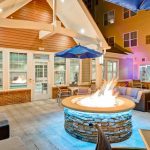 Outdoor patio with fire pit, lounge seating, and modern building backdrop at dusk.