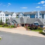 Large apartment complex under a bright blue sky with surrounding greenery and paved road.