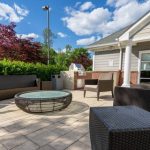 Outdoor patio with fire pit, seating area, and modern home backdrop on a sunny day.