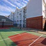 Outdoor basketball court with green and red surfaces, adjacent to a modern apartment building.