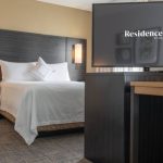 Modern hotel room with large bed, bedside lamps, and a wall-mounted TV displaying "Residence Inn by Marriott."