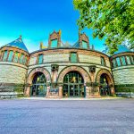 Victorian-style stone building with domes and arched entrances under a bright blue sky.
