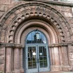 Ornate stone archway framing a modern glass entrance on an old building facade.