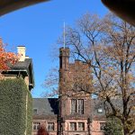 Gothic university building under a clear blue sky, framed by trees and architectural elements.