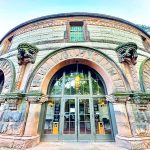 Stone facade of a historic, rounded building with large arched windows and entrance.