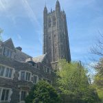 Gothic cathedral tower towering over historic stone building under a blue sky.
