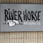 River Horse Brewing Co. logo displayed on a grey sign against a textured beige wall.