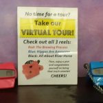 Sign promoting a virtual tour with three reels, flanked by two small toy cars.
