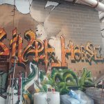Graffiti art featuring "SILPH HORSE" on a brick wall, with spray cans nearby.