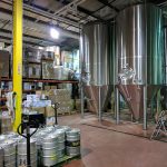 Large stainless steel storage tanks in a factory setting with stacked materials and industrial equipment.