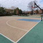 Outdoor basketball court with a partial view of surrounding park and buildings.