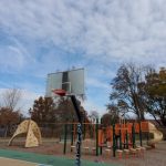 Outdoor basketball hoop and playground equipment under a partly cloudy sky.