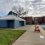 Blue building next to an empty outdoor pool under a cloudy sky.