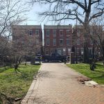 Brick apartment buildings line a brick walkway through a grassy, tree-lined courtyard.