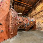 Indoor climbing gym with textured rock walls and industrial ceiling structure.