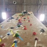 Climbing wall indoors with various colorful and black climbing holds on a brown surface.