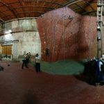Indoor climbing gym with massive, textured rock walls and high arched ceiling.