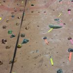 Bouldering wall with various colored climbing holds scattered across the textured surface.