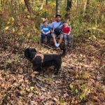 Family with black dog in an autumn forest setting.