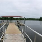 Wooden dock extending over calm water with a red canopy under an overcast sky.