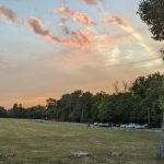 Sunset over a grassy field with trees lining the horizon and scattered clouds.