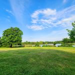Vast green lawn overlooking a calm lake under a bright blue, cloudy sky.