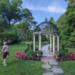Ornate iron gazebo in a lush, green garden with a pathway leading through it.