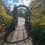 Stone pathway under a wrought iron archway leading into a park with trees.