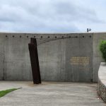 Concrete wall with quote, dark sculpture, and curving stone pathway under cloudy sky.