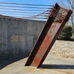 Rusty metal beam leaning against a concrete wall with barbed wire overhead.