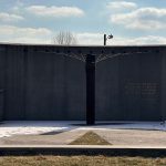 Concrete wall with a central dark pillar and overhead wires against a cloudy sky.
