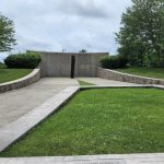 Memorial wall set in a grassy area surrounded by trees under an overcast sky.