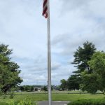 American flag flying on a tall flagpole in an outdoor park setting under cloudy skies.