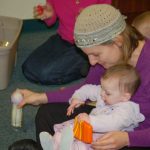 Woman in purple shirt and patterned hat interacts with a baby during an activity.