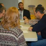 Group of men and women gathered around a table in a meeting or study setting.
