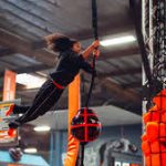 Woman rappelling down a rope inside an industrial or warehouse setting.